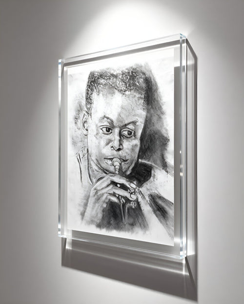A framed black and white portrait drawing of a man playing an instrument, displayed in a clear acrylic shadow-box frame against a light gray wall with dramatic spotlighting.